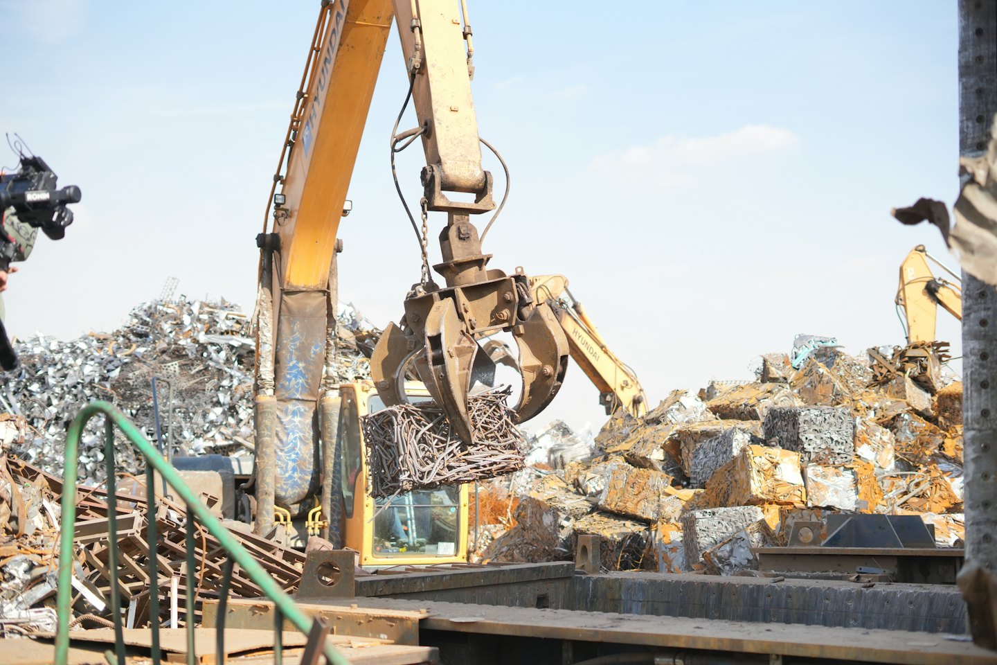 Yellow grapple loader lifting a cube of scrap metal.